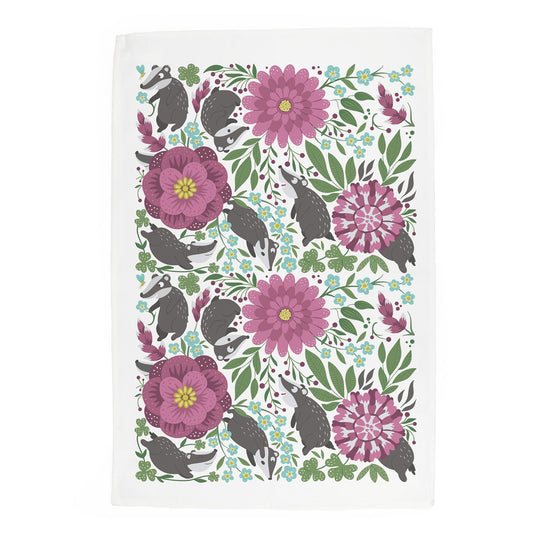 Pattern design featuring cute cartoon badgers nestled amongst green leaves & pretty wildflowers on a cotton tea towel